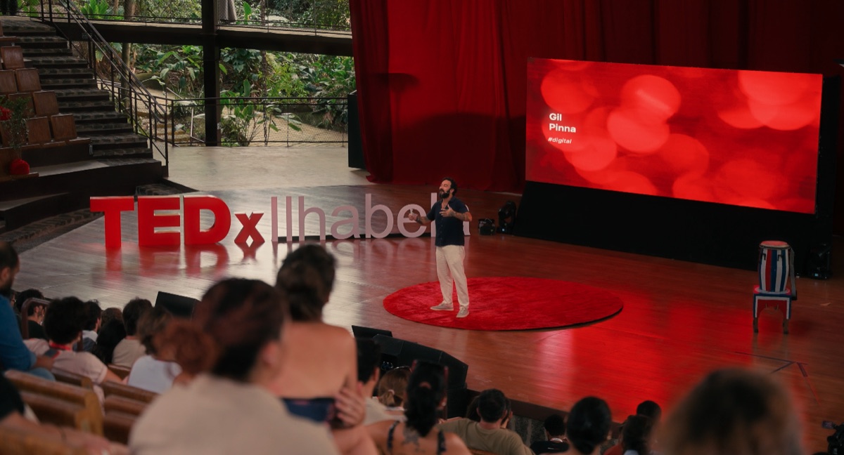 Gil Pinna palestrando no palco com letreiro TEDxIlhabela e cortina vermelha